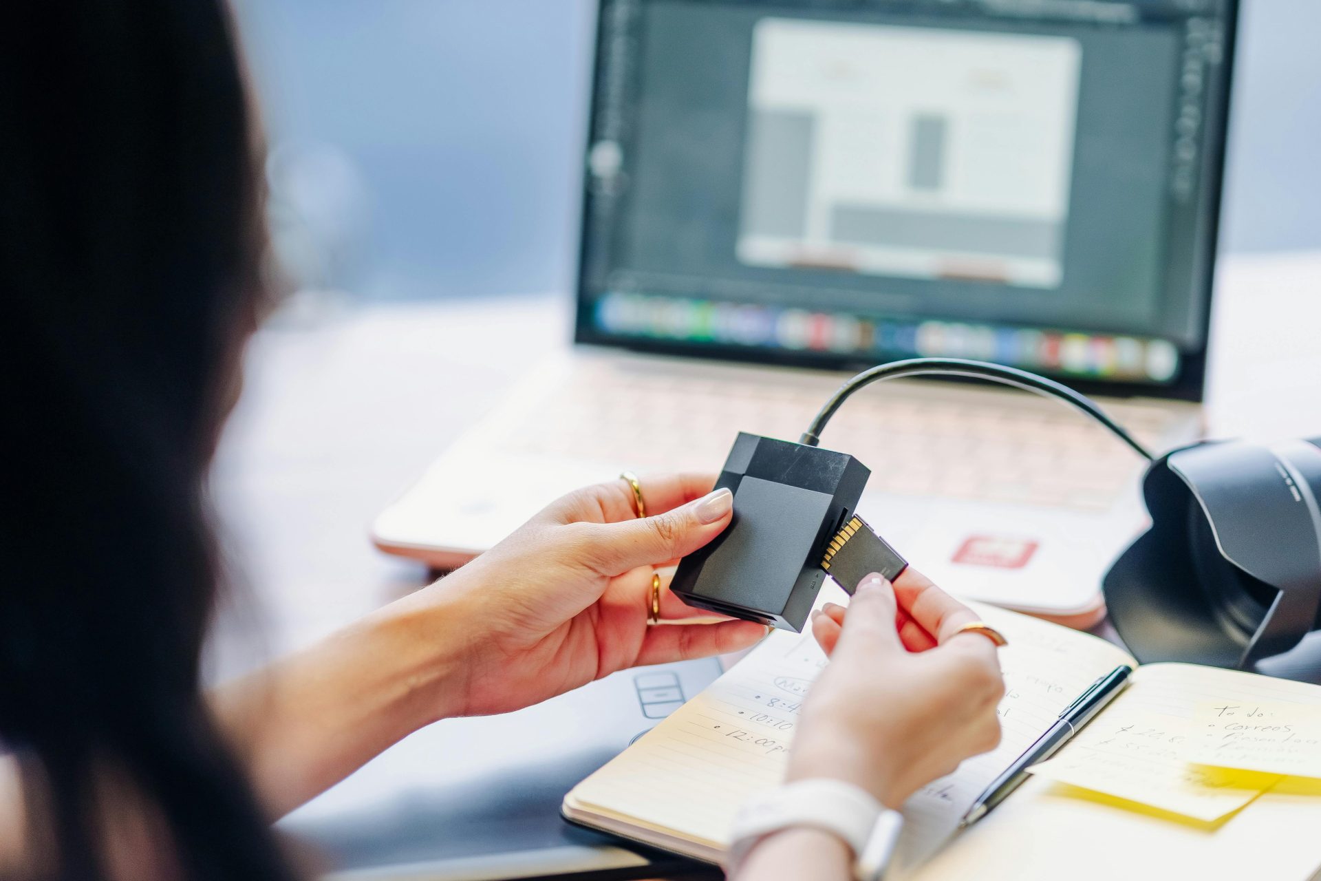 Gros plan sur des mains utilisant un lecteur de carte mémoire connecté à un ordinateur portable, illustrant les éléments essentiels du travail numérique.